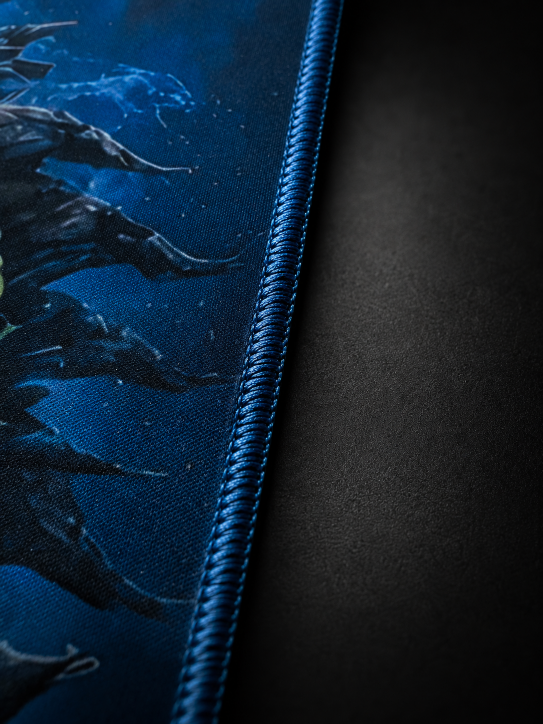 Jormungandr gaming mousepad stitched edge detail on a dark gray background, highlighting premium blue border stitching and textured cloth surface.