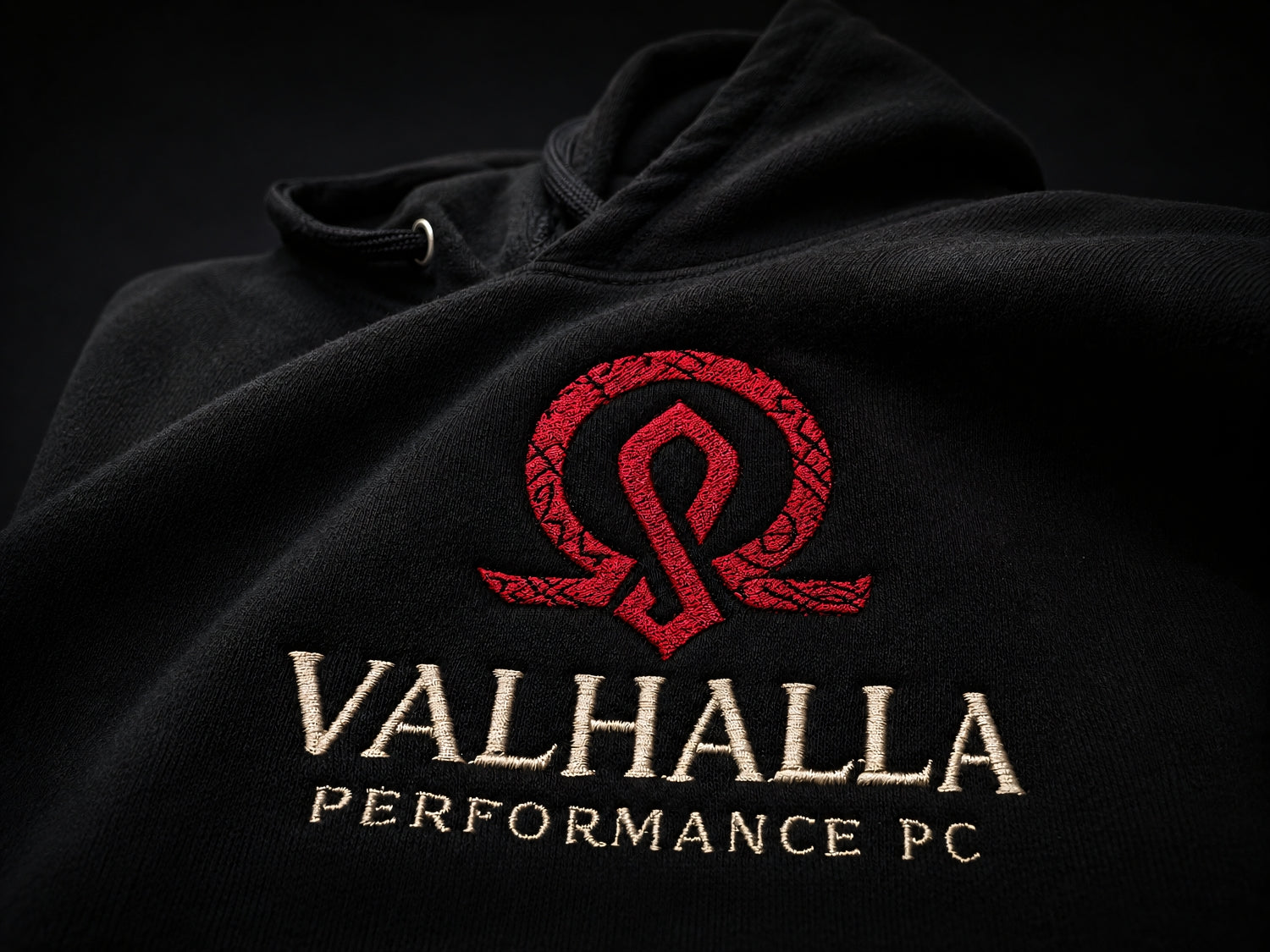 Close-up of the Valhalla Forged Fleece Hoodie embroidered chest logo on black fleece fabric.